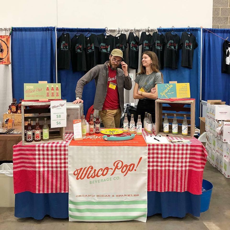 Custom printed table cover with Wisco Pop Beverage Co. branding at trade show booth featuring organic sodas