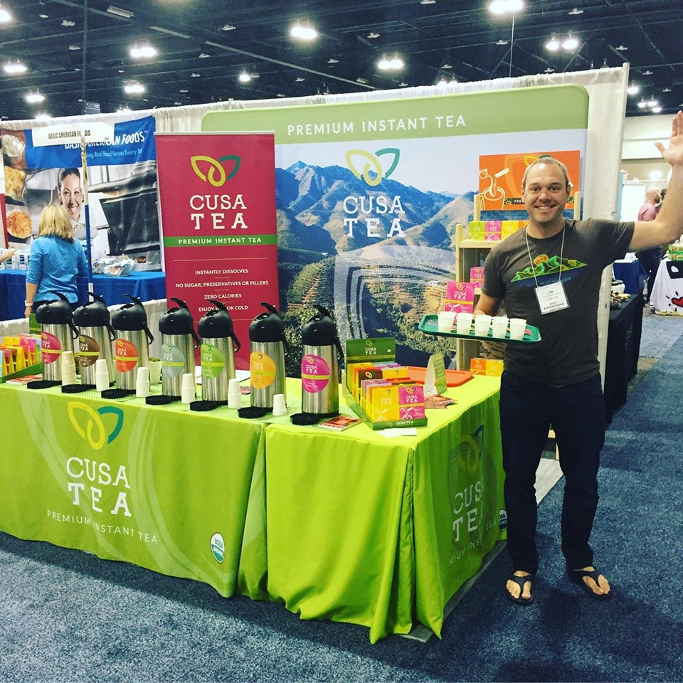 Custom table covers for Cusa Tea trade show booth with product samples and branded instant tea display