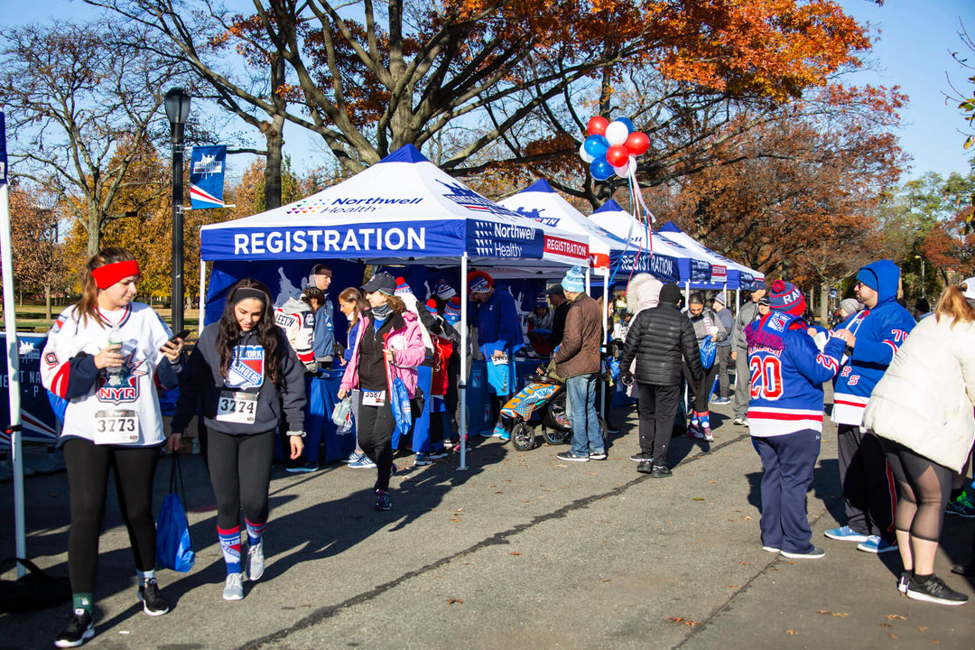 Participants register under custom canopy tents at a 5K run event, organized by the NY Rangers, on a crisp autumn day