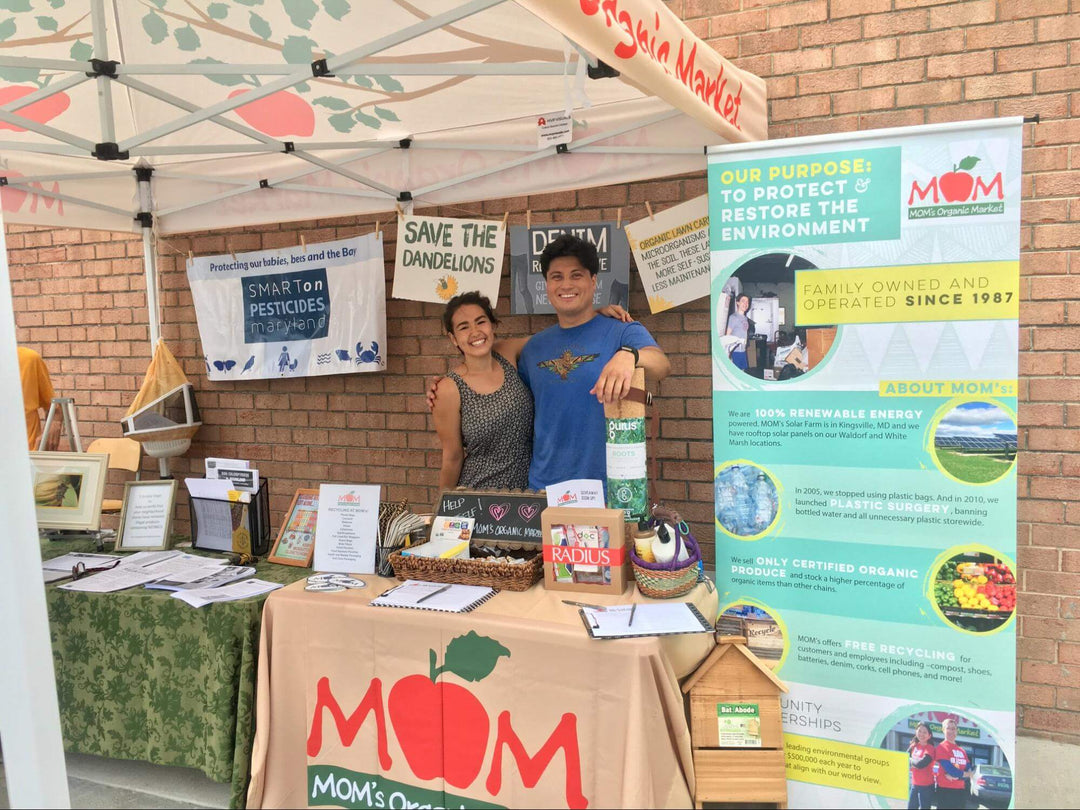Smiling vendors at a custom farmers market pop-up tent with information banners, promoting organic products