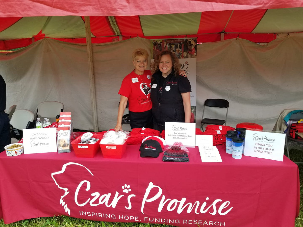 Two women standing behind a table with 'Czar's Promise' branding at an event.