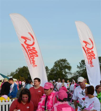 White feather flags with red “Dillons” logo at a breast cancer awareness event with participants in pink and white attire.