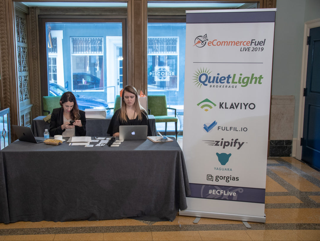 eCommerceFuel Live 2019 registration table with roll up banner displaying sponsor logos including Quiet Light, Klaviyo, and Gorgias