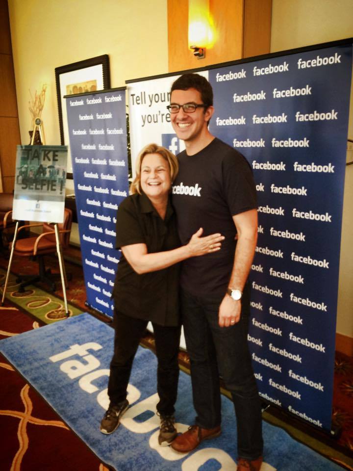 Two people posing and smiling in front of branded Facebook roll up banners and carpet at a selfie station setup.