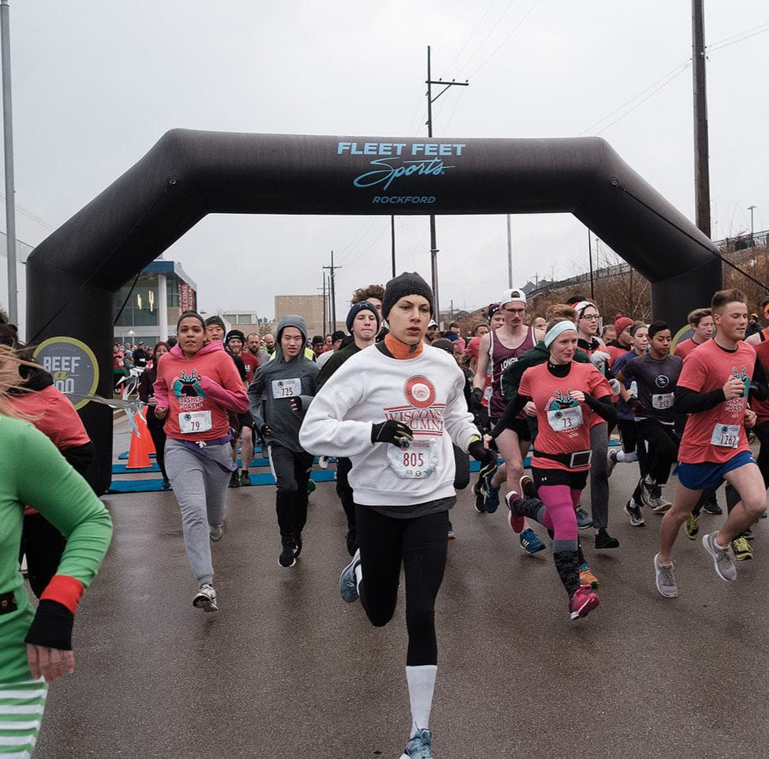 Runners in festive gear starting a holiday race under a custom black inflatable arch branded for Fleet Feet Rockford, produced by MVP Visuals