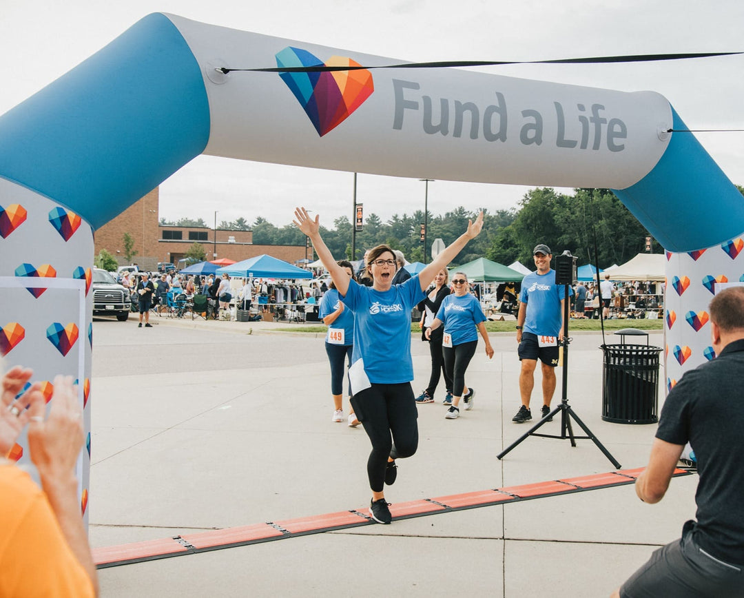 Participant celebrating at the finish line under a custom inflatable arch with Fund a Life heart logo during a charity event