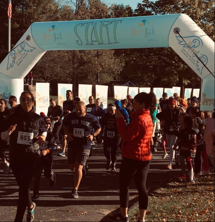 Runners beginning a charity race under a custom white inflatable arch with Happy Jack Fund branding and illustrated angel wings