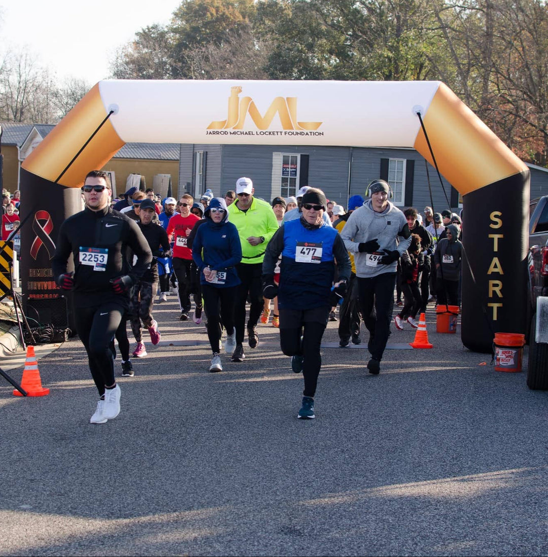 Runners taking off from the start line under a custom inflatable arch featuring Jarrod Michael Lockett Foundation branding at a community race, made by MVP Visuals