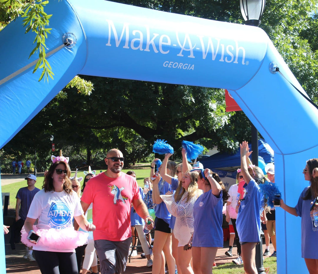 Participants and volunteers celebrating under a bright blue inflatable arch with Make-A-Wish Georgia branding during a community walk event
