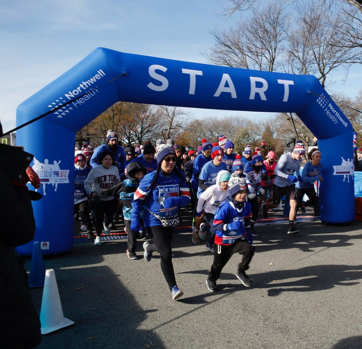 Participants launching from the start line under a custom blue inflatable arch for the New York Rangers 5K sponsored by Northwell Health