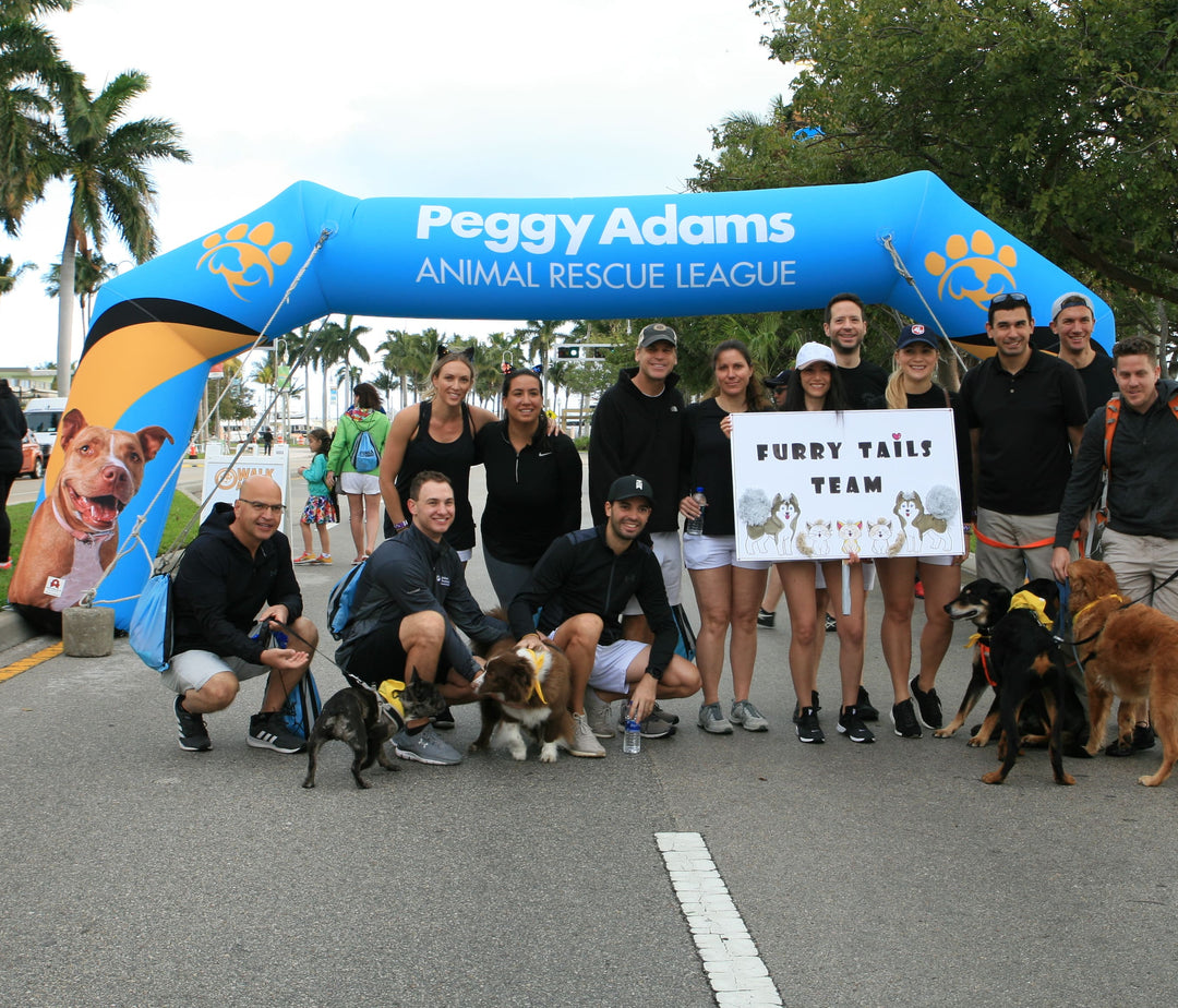 Furry Tails Team posing with dogs under a custom inflatable arch for Peggy Adams Animal Rescue League during a pet adoption and charity walk event