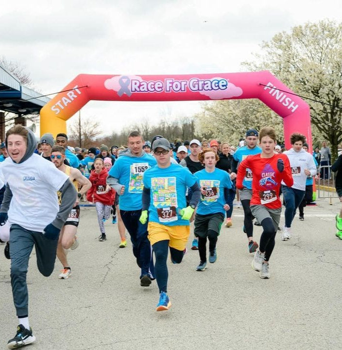 Participants starting a community charity run under a colorful inflatable arch with Race For Grace branding and start-finish signage