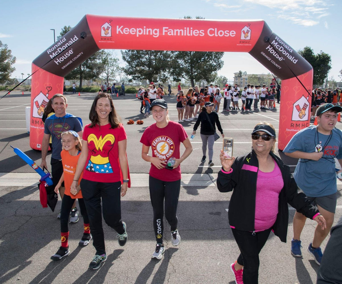 Families and participants walking under a red inflatable arch with Ronald McDonald House Orange County branding during a community charity event
