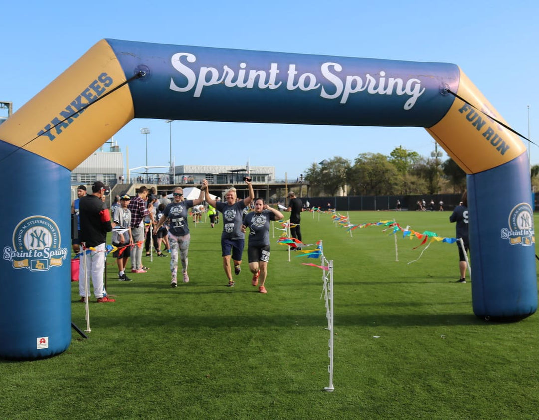 Participants crossing the finish line under a custom inflatable arch with New York Yankees Sprint to Spring Fun Run branding on a baseball field