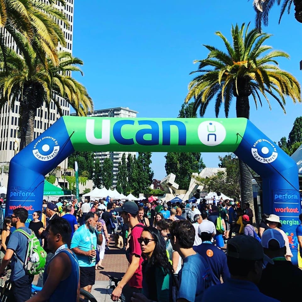 Crowds walking through a custom inflatable arch branded with UCAN and SuperStarch at a large outdoor expo or fitness event