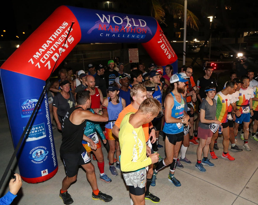 International marathon participants lined up at the start line under a custom inflatable arch for the World Marathon Challenge event