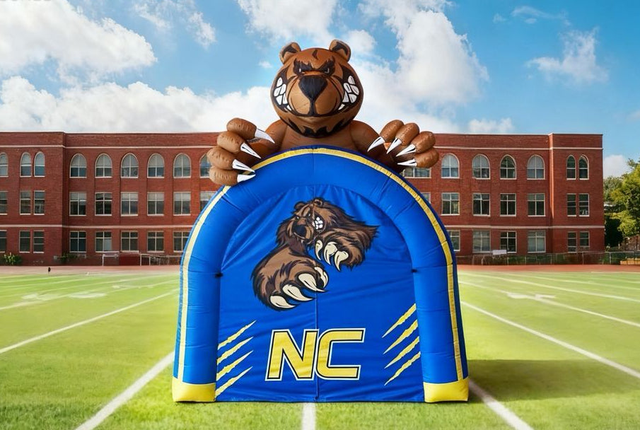 Inflatable bear mascot with 'NC' on a football field, building in the background