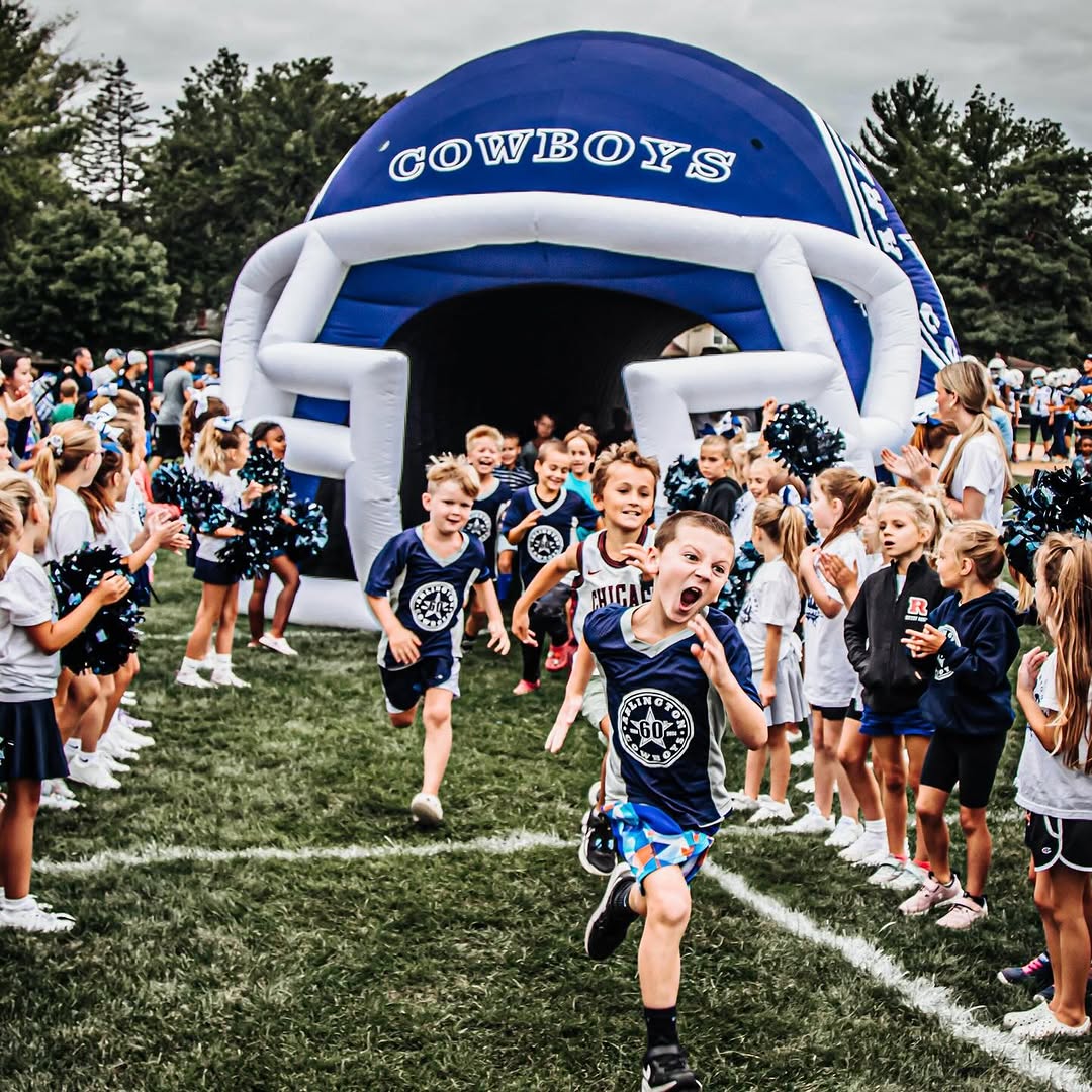 Kids running out of inflatable Cowboys helmet tunnel during pep rally