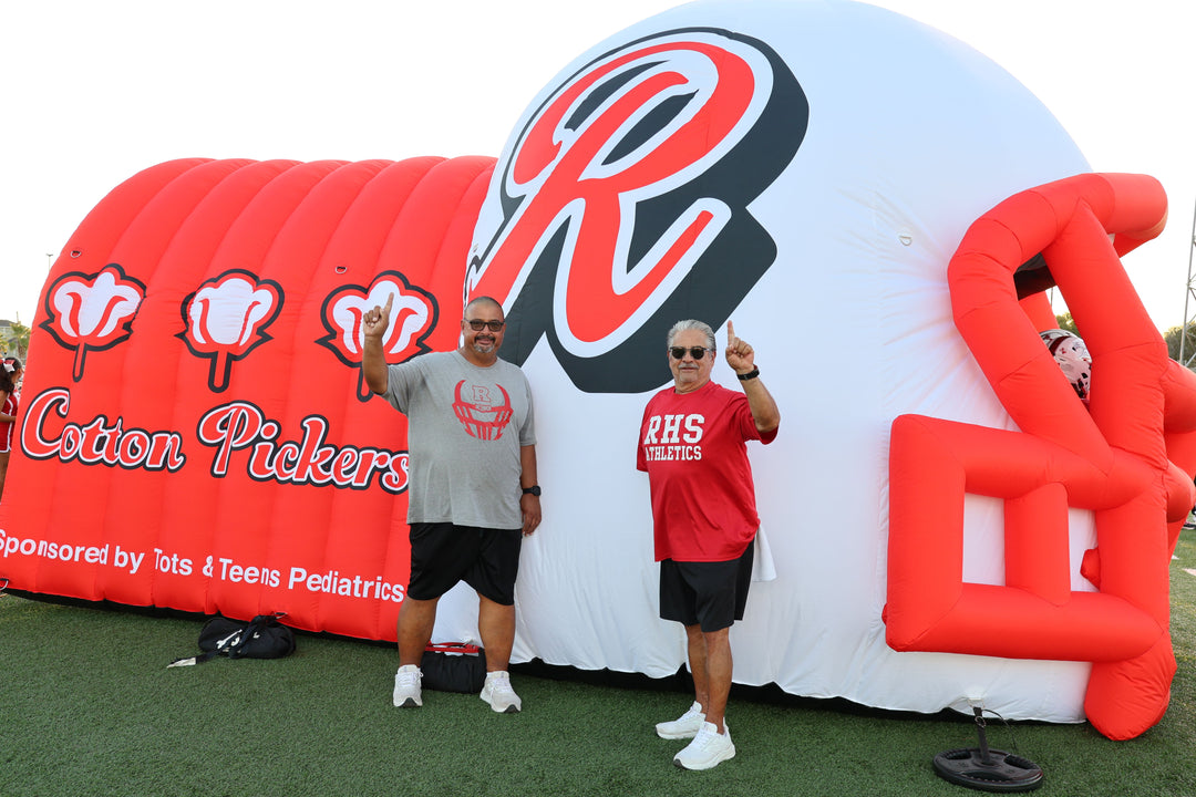 Inflatable football helmet tunnel for Cotton Pickers team with two coaches posing in front.