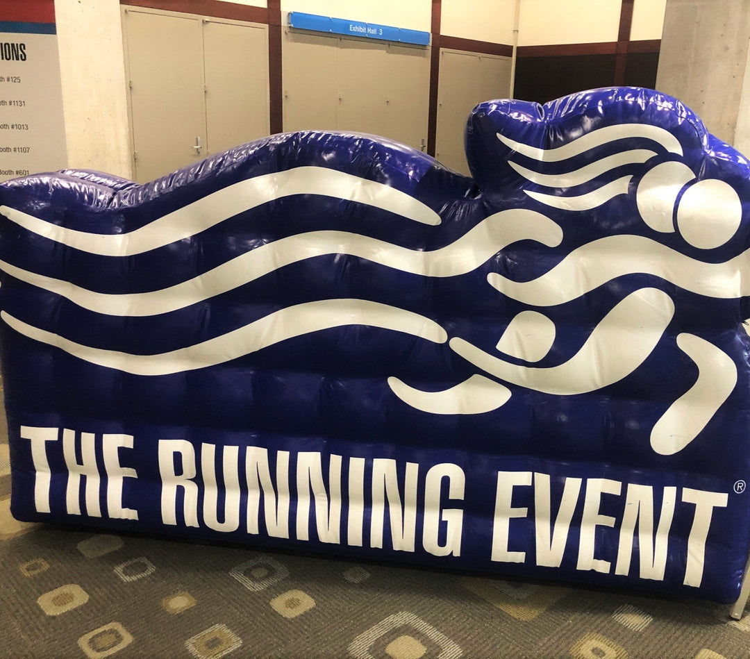 Inflatable logo display for The Running Event featuring stylized runner graphic in blue and white