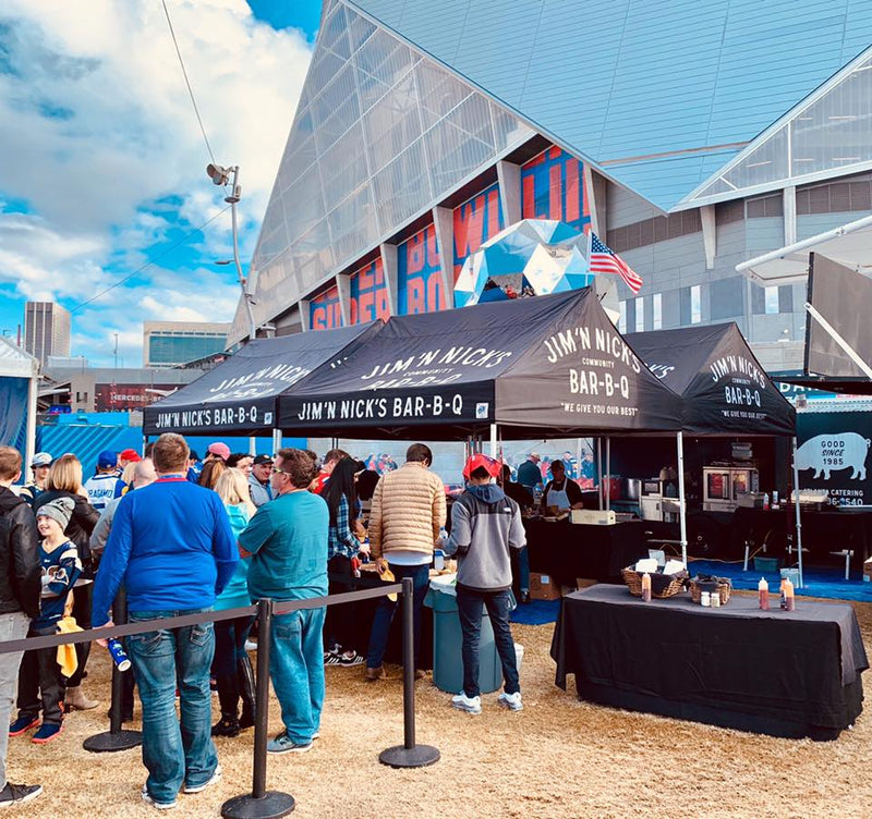 Jim ‘N Nick’s BBQ 10x15 custom canopy tent setup at stadium event with crowd and branded outdoor food booth