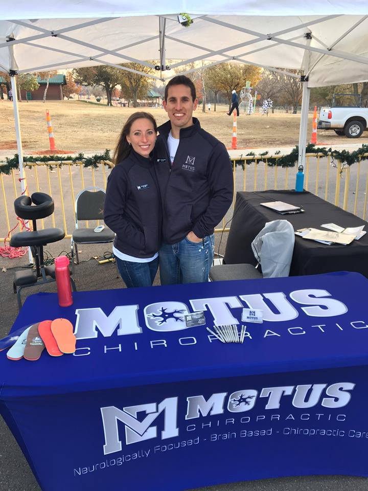 Two people standing behind a blue M1 Motus Chiropractic table outdoors.