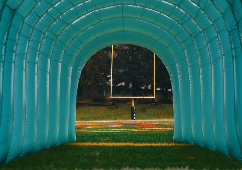 Custom blue inflatable football tunnel on a field with goalposts visible through the archway, capturing the anticipation of game day