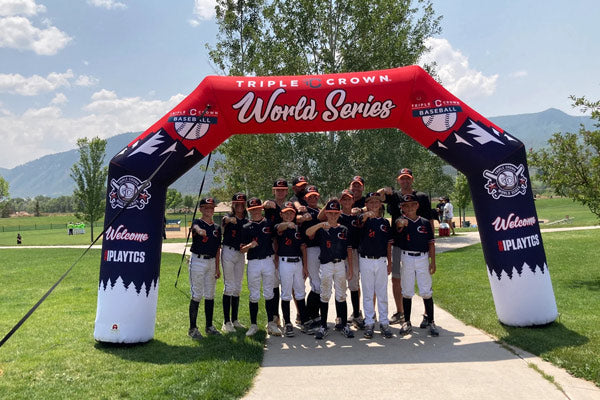 Youth baseball team posing under a Triple Crown World Series inflatable archway at a sports event.