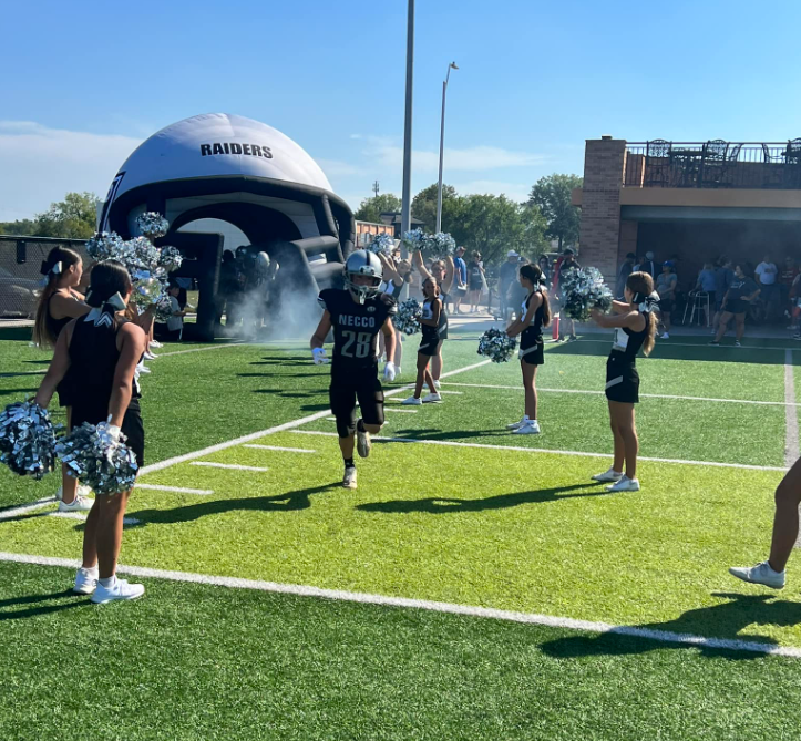 youth football player runs through inflatable tunnel with cheerleaders on both sides