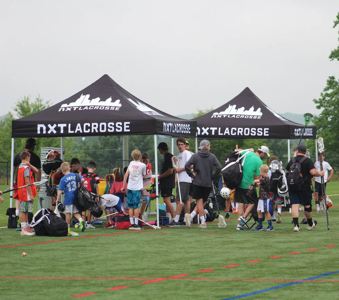 NXT Lacrosse custom canopy tents at youth sports camp with players gathering on field