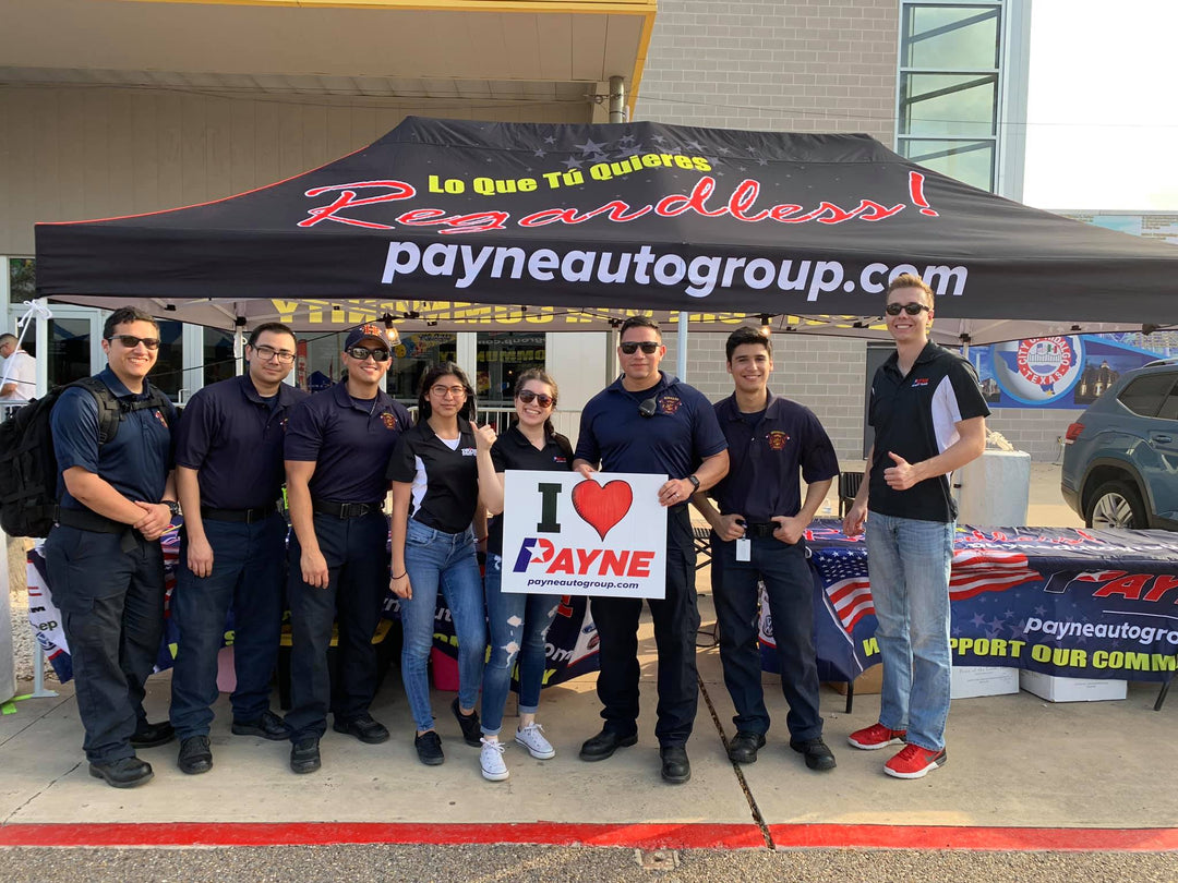 Payne Auto Group team and local fire department staff pose in front of branded tent at community outreach event.