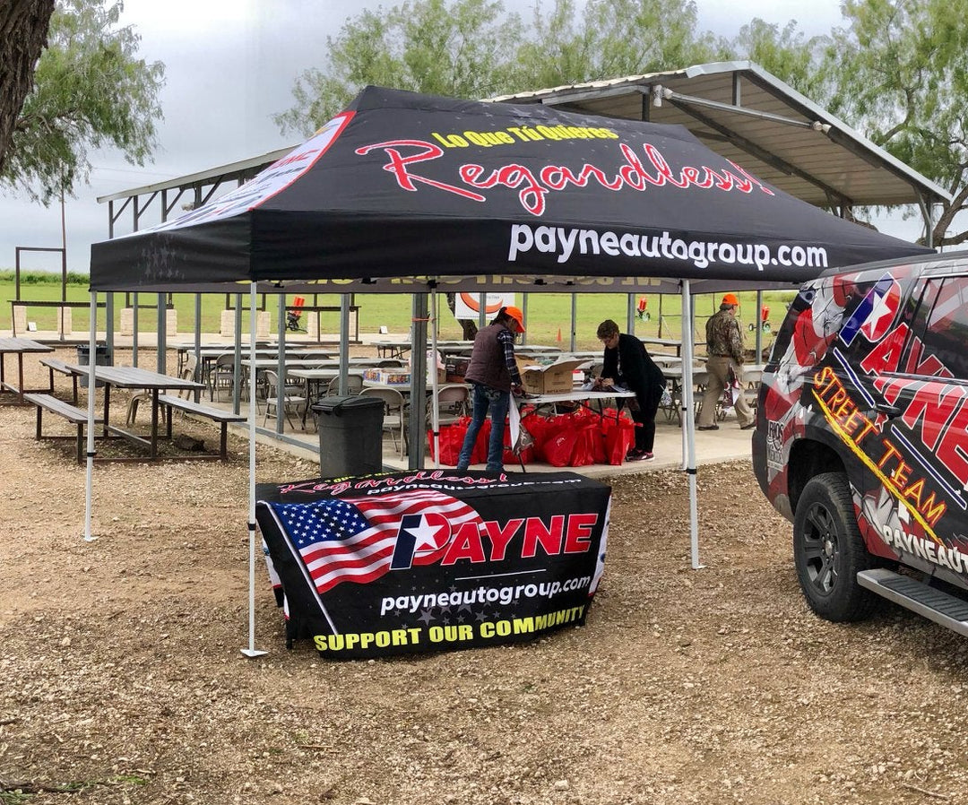 Branded Payne Auto Group SUV and canopy tent setup at outdoor community event with tables and volunteers under pavilion.