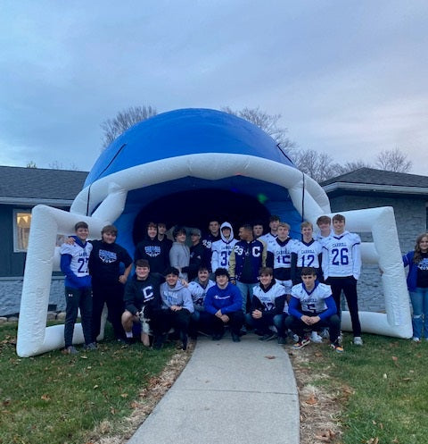high school football team posing in front of blue and white inflatable helmet tunnel