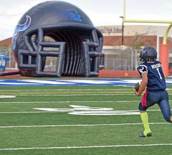 Youth football player runs toward inflatable helmet tunnel labeled "Rampage" during game