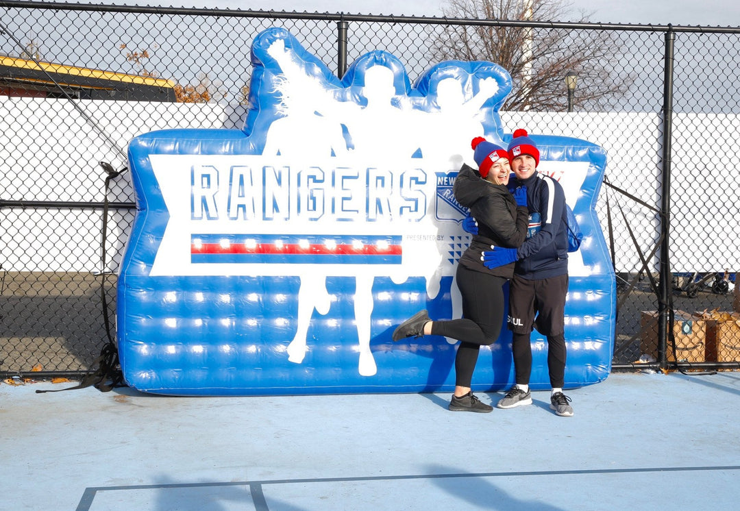 Couple poses in front of blue inflatable Rangers 5K backdrop with silhouettes of runners