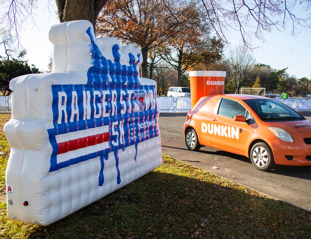 Inflatable Rangerstown 5K sign next to branded Dunkin’ car and coffee cup at outdoor event