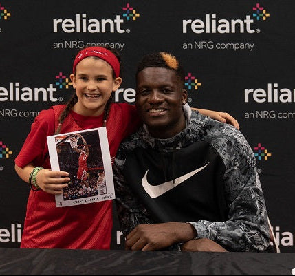 Young fan posing with professional basketball player Clint Capela in front of a branded Reliant vinyl banner at a meet-and-greet event.