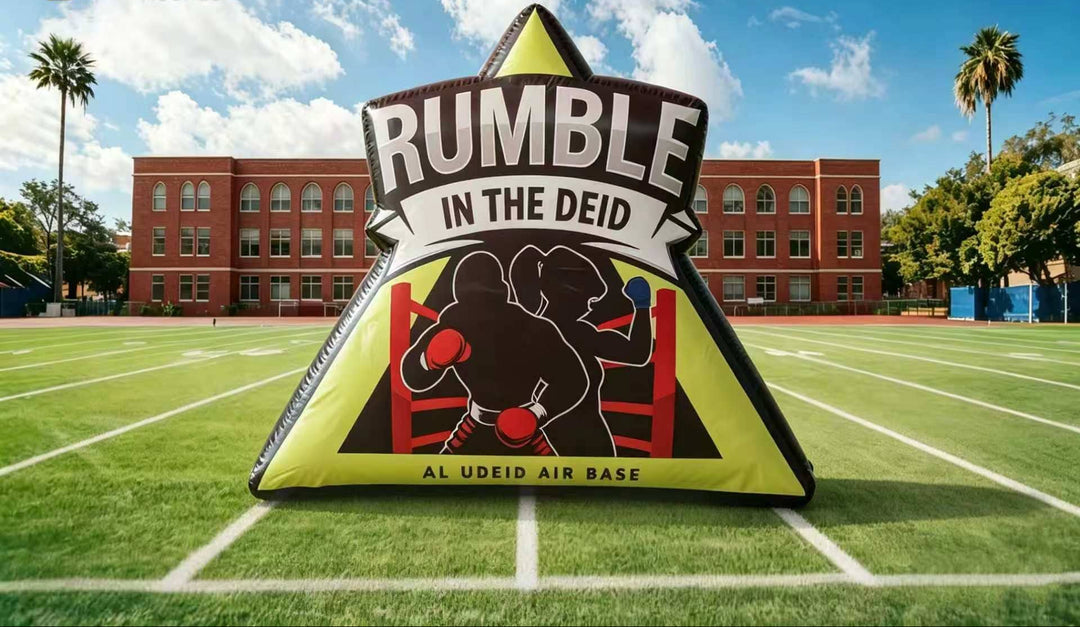 Inflatable 'Rumble in the Deid' sign on a sports field with a building and palm trees in the background.