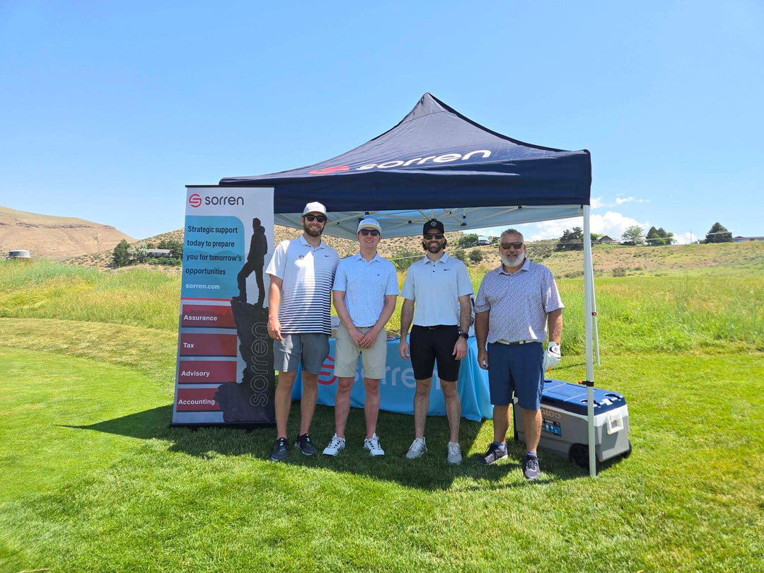 Four men posing in front of Sorren accounting booth at a sunny outdoor golf event