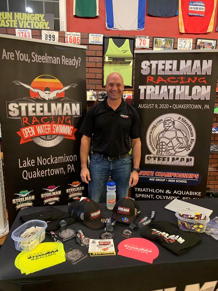 Steelman Racing triathlon event booth with promotional roll up banners, medals, and merchandise display