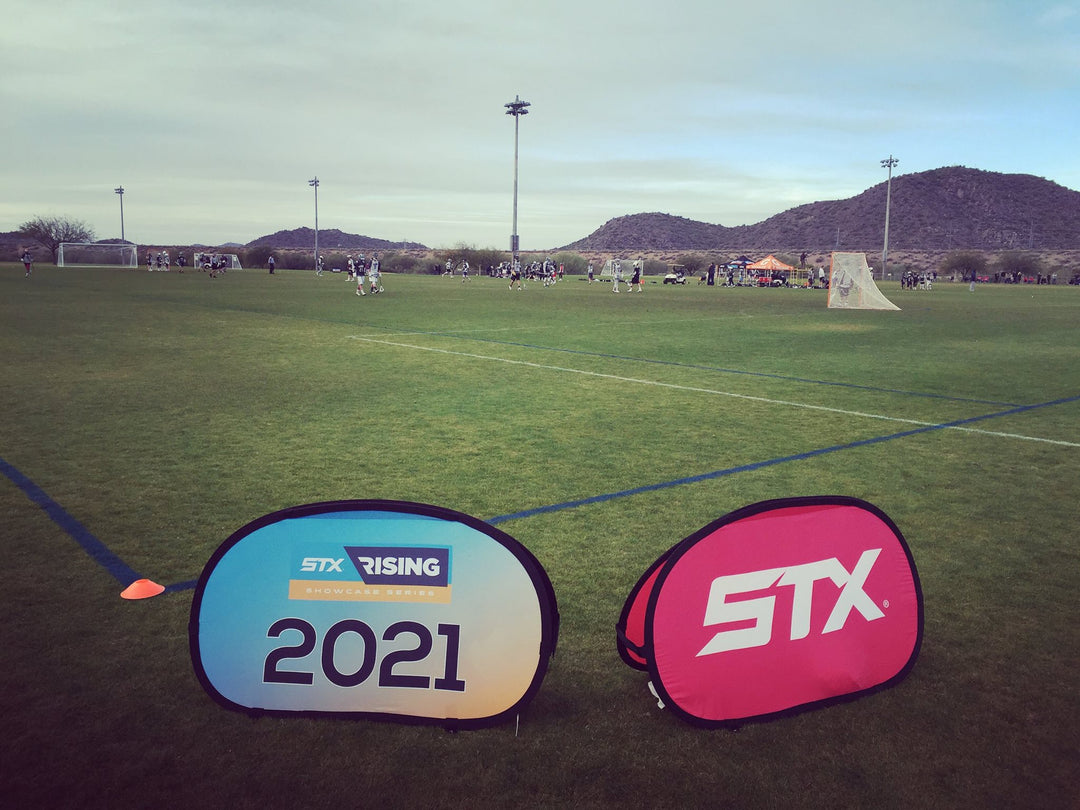 STX Rising 2021 and STX branded pop-up banners on a lacrosse field with players and mountains in the background