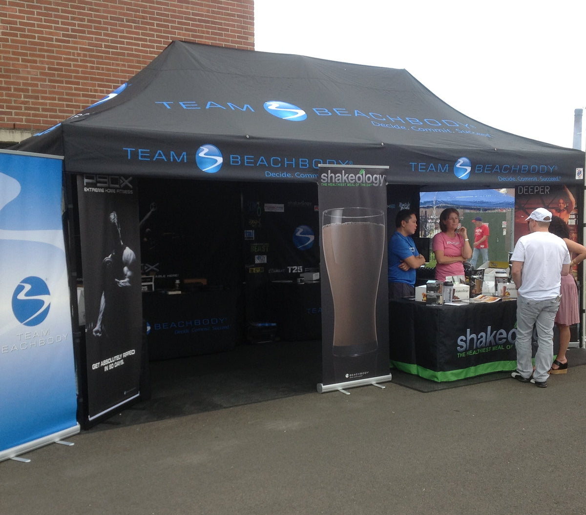 Branded canopy tent for Team Beachbody with Shakeology banners and staff engaging attendees at outdoor event