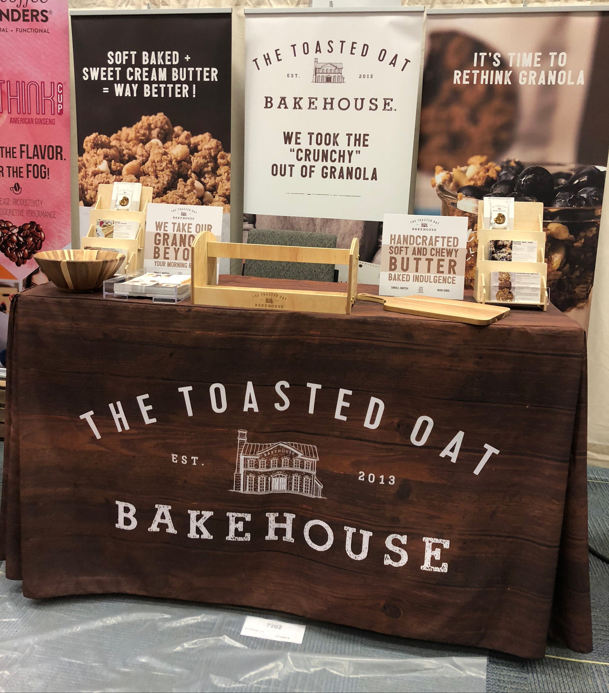 Display of The Toasted Oat Bakehouse products with branded tablecloth and posters.