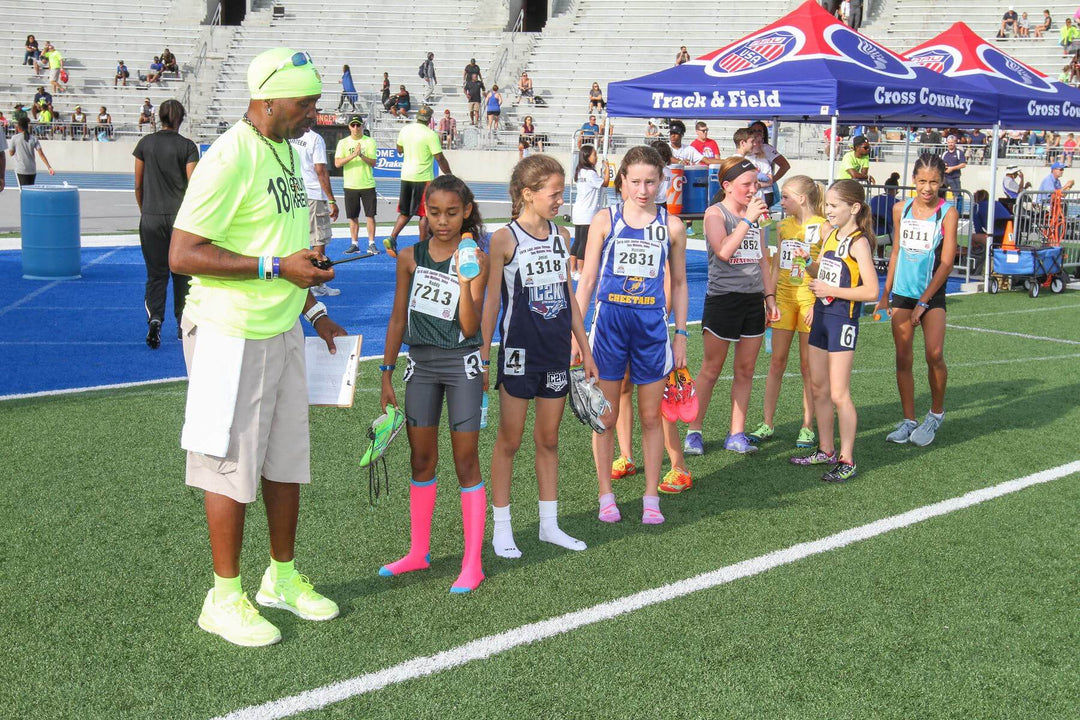 A vibrant track and field tent at a meet, with young athletes and a coach on a blue track