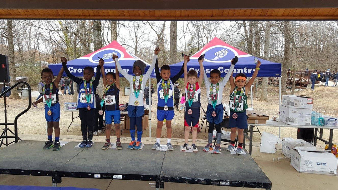 Youth athletes on a podium under a cross country tent, proudly displaying medals in a park setting