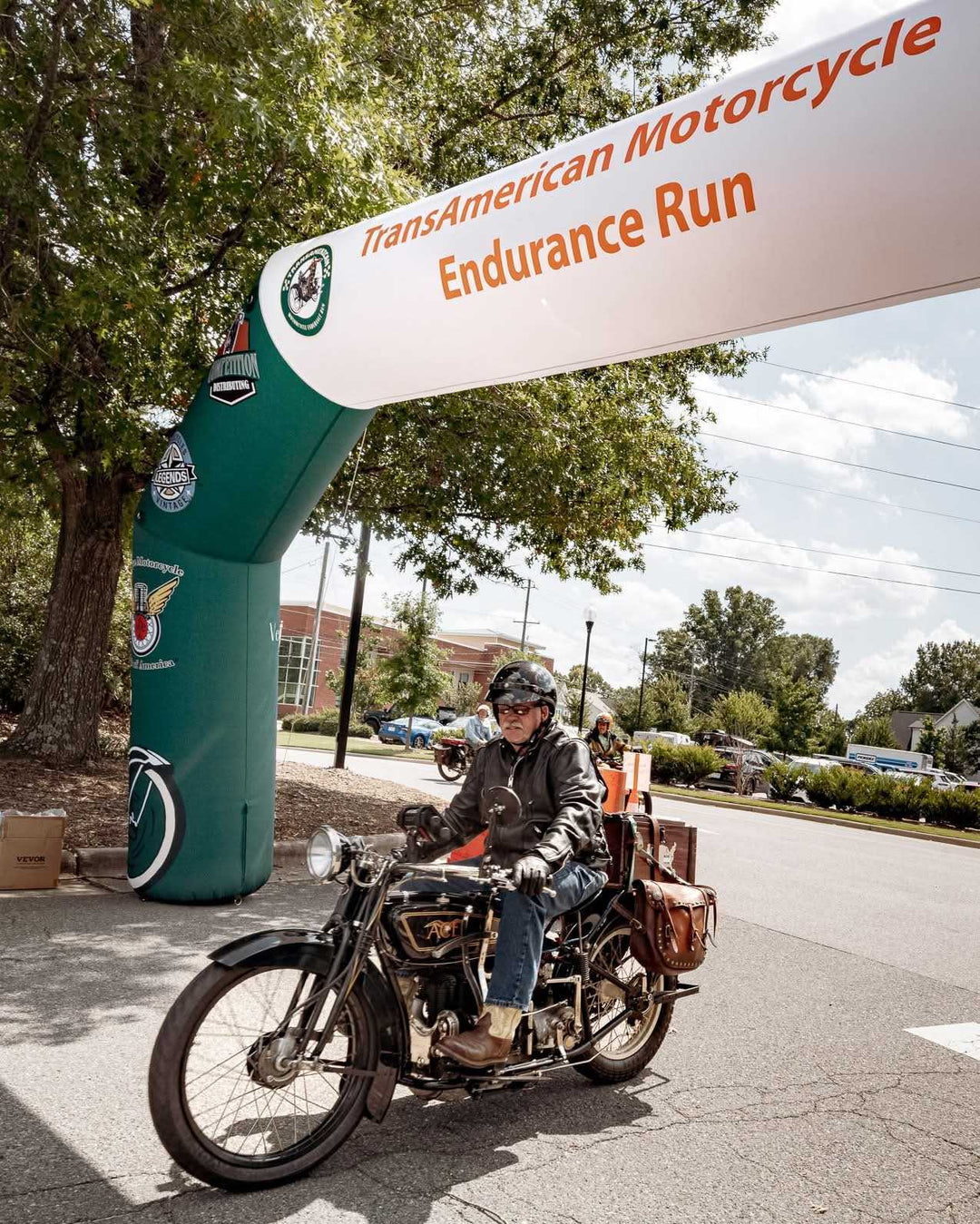 Motorcyclist rides vintage bike through "TransAmerican Motorcycle Endurance Run" inflatable archway during a scenic event