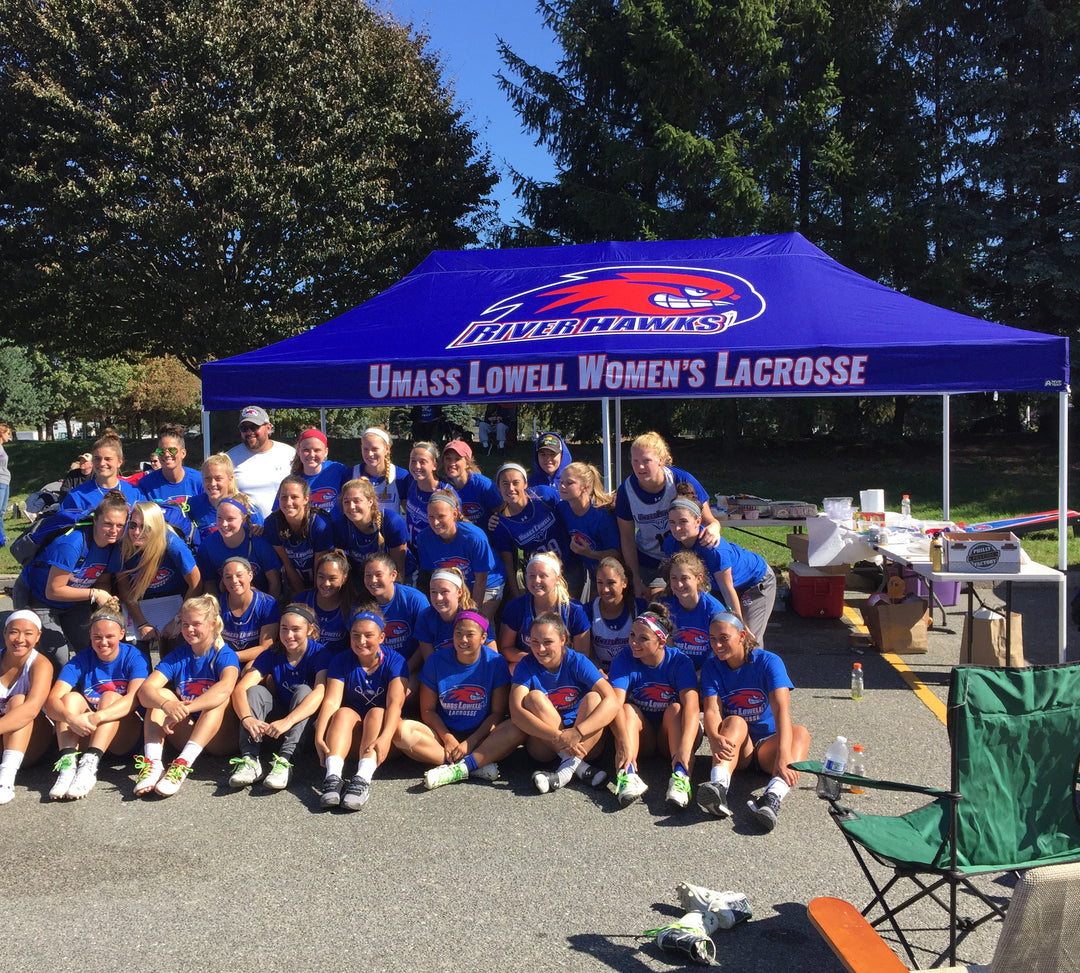 UMass Lowell Women’s Lacrosse team posing under custom River Hawks canopy at outdoor team event