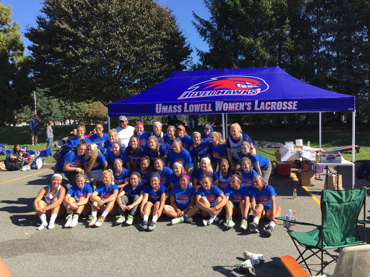 UMass Lowell Women’s Lacrosse team posing under custom River Hawks canopy at outdoor team event