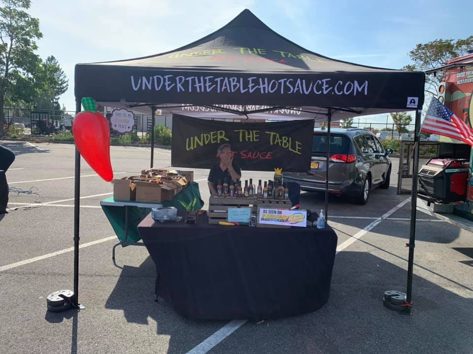 Under The Table Hot Sauce custom canopy tent with branded market booth and product display at outdoor vendor event