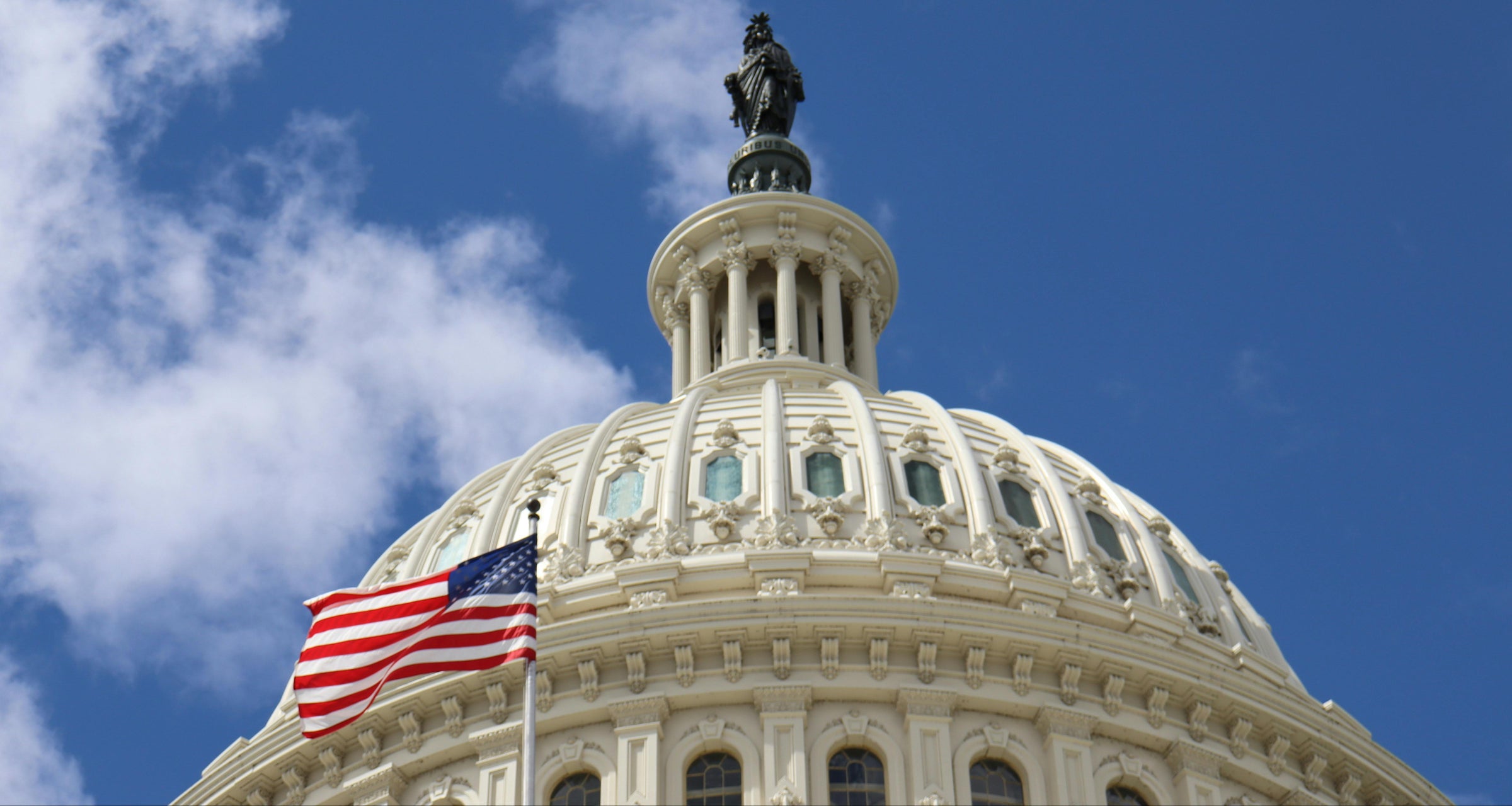 U.S. Capitol dome with American flag against a blue sky